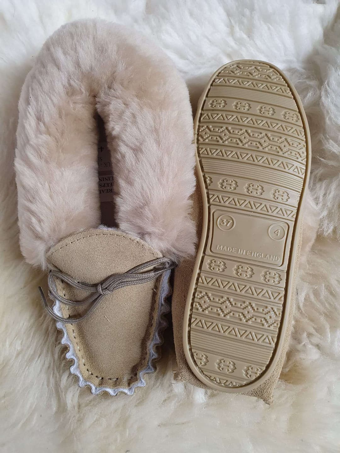 A beige pair of slippers, with a sheo lace